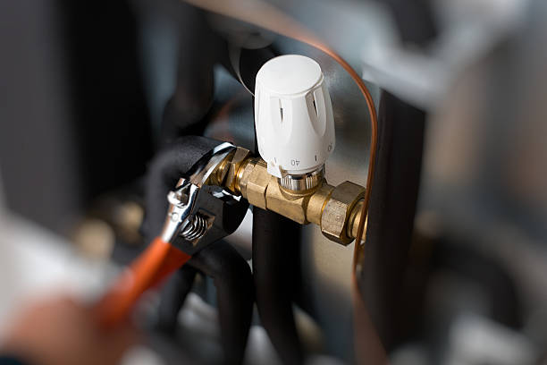 The image shows the dial and pipe of a boiler being adjusted with a wrench.